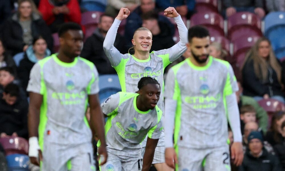 Manchester City forward Erling Haaland (center) celebrates with his arms raised after scoring the decisive goal in a 1-0 victory against Burnley at Turf Moor on April 22, 2026. He is joined in the foreground by teammates Jérémy Doku (front center), who provided the assist. Image used for Sportxparte news.