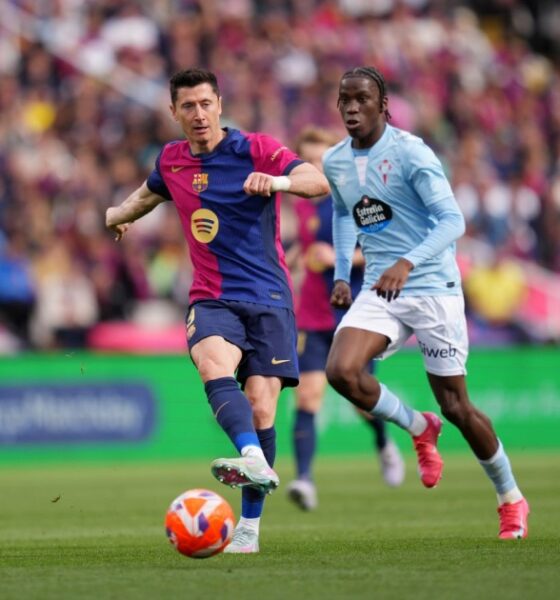 Robert Lewandowski, in a dark blue and red FC Barcelona kit, shields the ball and prepares to strike while being closely pursued by Ilaix Moriba in a light blue Celta Vigo jersey during a La Liga match at a crowded stadium. Image used for Sportxparte news.