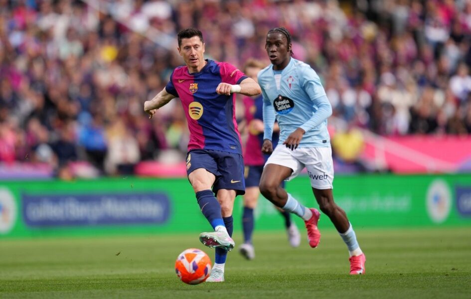 Robert Lewandowski, in a dark blue and red FC Barcelona kit, shields the ball and prepares to strike while being closely pursued by Ilaix Moriba in a light blue Celta Vigo jersey during a La Liga match at a crowded stadium. Image used for Sportxparte news.