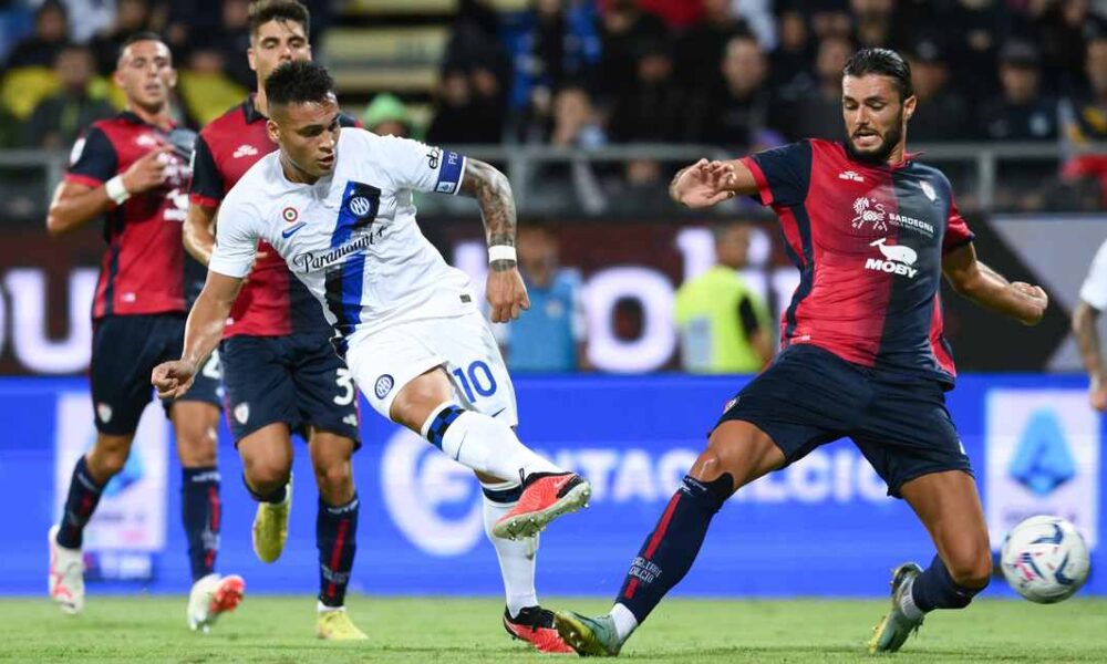 Inter Milan forward Lautaro Martínez, wearing a white away kit with the number 10, strikes a low shot toward the goal while Cagliari defender Alberto Dossena slides in to block during a Serie A football match at the Sardegna Arena. Image used for Sportxparte news.