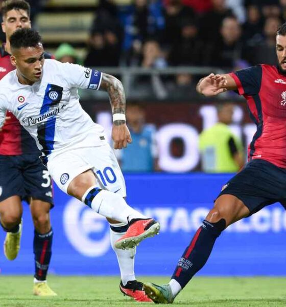 Inter Milan forward Lautaro Martínez, wearing a white away kit with the number 10, strikes a low shot toward the goal while Cagliari defender Alberto Dossena slides in to block during a Serie A football match at the Sardegna Arena. Image used for Sportxparte news.