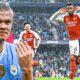 An action-oriented promotional graphic featuring Erling Haaland of Manchester City on the left, looking intense and celebrating, and Gabriel Magalhães of Arsenal on the right, running and celebrating a goal. In the background, another Arsenal player is visible on the pitch in a crowded stadium during a rainy match day. The Premier League logo is positioned in the top left corner. Image used for Sportxparte news.
