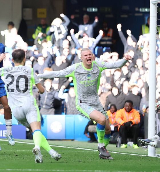 Manchester City's Nico O'Reilly celebrates with high energy after scoring the opening goal during the Premier League match against Chelsea at Stamford Bridge on April 12, 2026. The young midfielder is shown in City's grey and yellow away kit, with the Chelsea goal and reacting players visible in the background. Image used for Sportxparte news