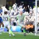 Manchester City's Nico O'Reilly celebrates with high energy after scoring the opening goal during the Premier League match against Chelsea at Stamford Bridge on April 12, 2026. The young midfielder is shown in City's grey and yellow away kit, with the Chelsea goal and reacting players visible in the background. Image used for Sportxparte news