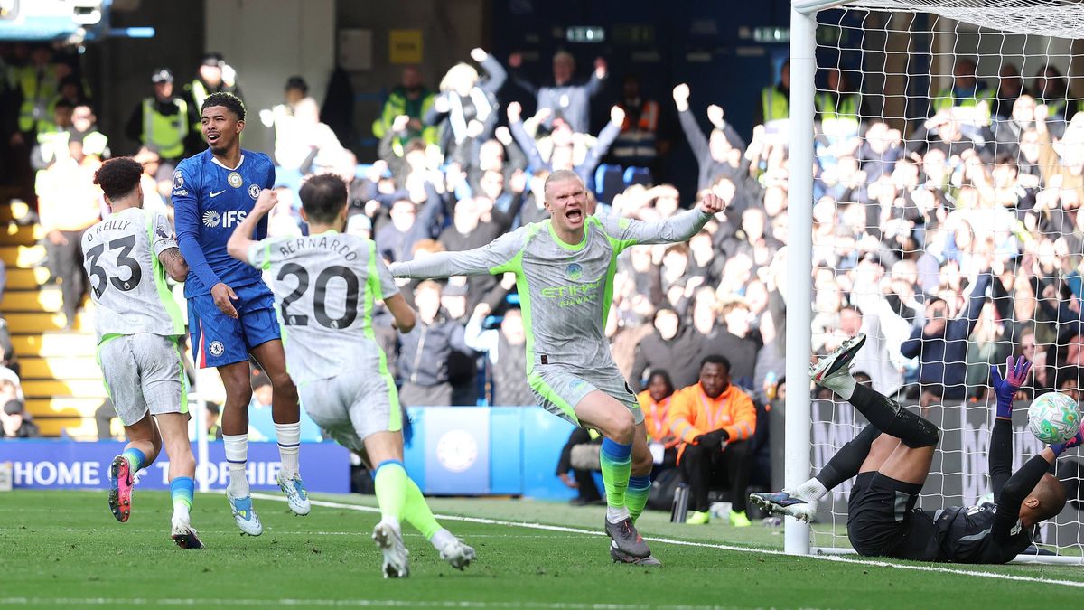 Manchester City's Nico O'Reilly celebrates with high energy after scoring the opening goal during the Premier League match against Chelsea at Stamford Bridge on April 12, 2026. The young midfielder is shown in City's grey and yellow away kit, with the Chelsea goal and reacting players visible in the background. Image used for Sportxparte news