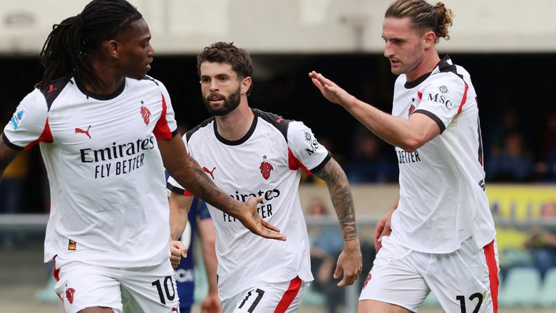 Three AC Milan players, Rafael Leão (#10), Christian Pulisic (#11), and Adrien Rabiot (#12), celebrate on the pitch during a Serie A match against Hellas Verona. They are wearing the club's white 2025-26 PUMA away kit. Rafael Leão is on the left, looking toward his teammates; Christian Pulisic is in the center; and Adrien Rabiot is on the right with his arm raised in celebration. Image used for Sportxparte news.