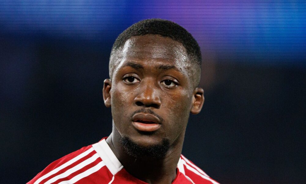 French professional footballer Ibrahima Konaté, looking slightly off-camera with a focused expression. He is wearing a red and white Liverpool F.C. training or kit jersey against a blurred, dark blue background. Image used for Sportxparte news.