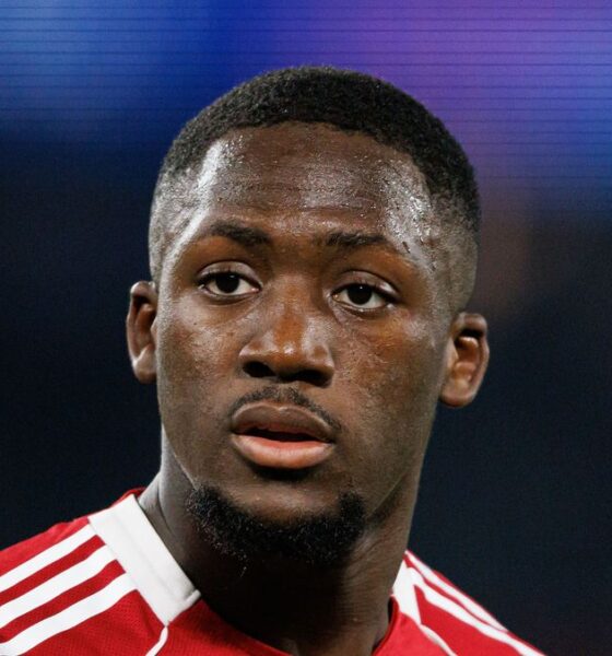 French professional footballer Ibrahima Konaté, looking slightly off-camera with a focused expression. He is wearing a red and white Liverpool F.C. training or kit jersey against a blurred, dark blue background. Image used for Sportxparte news.