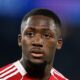 French professional footballer Ibrahima Konaté, looking slightly off-camera with a focused expression. He is wearing a red and white Liverpool F.C. training or kit jersey against a blurred, dark blue background. Image used for Sportxparte news.