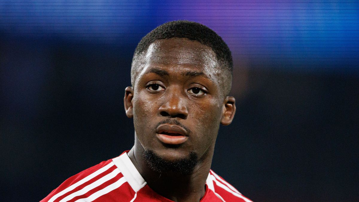 French professional footballer Ibrahima Konaté, looking slightly off-camera with a focused expression. He is wearing a red and white Liverpool F.C. training or kit jersey against a blurred, dark blue background. Image used for Sportxparte news.