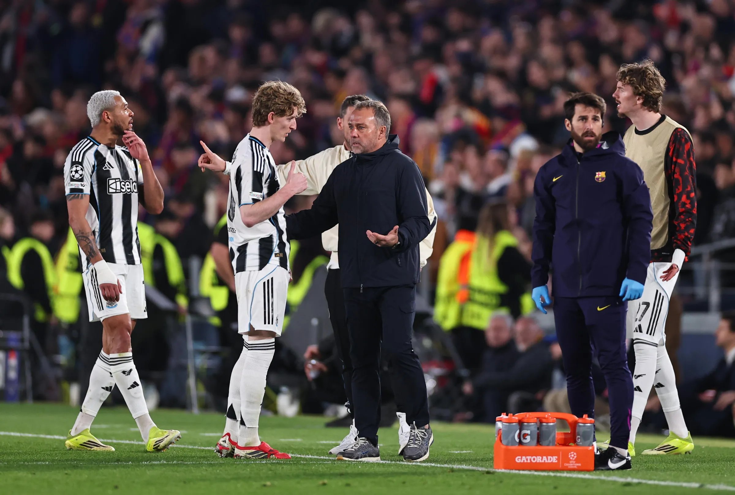 Newcastle United player Anthony Gordon speaking with FC Barcelona head coach Hansi Flick on March 18, 2026, during a UEFA Champions League match at Camp Nou. Image used for Sportxparte news.