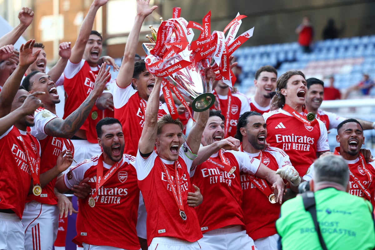 Arsenal captain Martin Ødegaard hoisting the Premier League trophy surrounded by his ecstatic teammates following the final match of the 2025–26 season. Image used for Sportxparte news.
