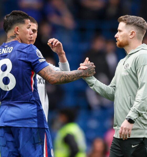 Chelsea midfielder Enzo Fernández (wearing the blue number 8 jersey) shakes hands and converses with interim head coach Calum McFarlane (in a grey Chelsea training hoodie) on a football pitch during a match day. Image used for Sportxparte news.