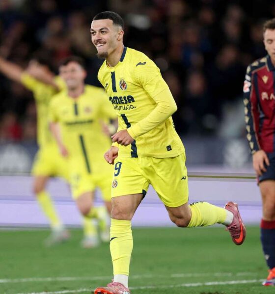 Georges Mikautadze is celebrating a goal for Villarreal CF. He is wearing a bright yellow kit and is captured mid-run with a joyful expression and clenched fists. In the background, teammates in yellow and an opposing player in a navy and maroon kit look on. Image used for Sportxparte Preview.