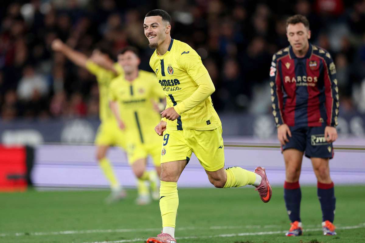 Georges Mikautadze is celebrating a goal for Villarreal CF. He is wearing a bright yellow kit and is captured mid-run with a joyful expression and clenched fists. In the background, teammates in yellow and an opposing player in a navy and maroon kit look on. Image used for Sportxparte Preview.