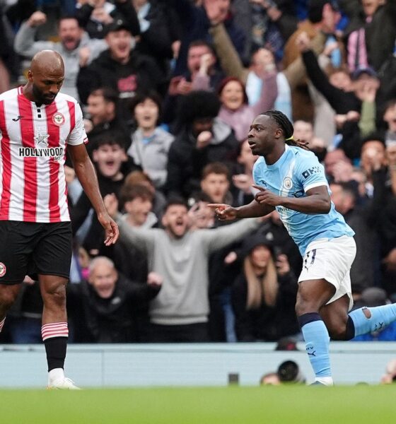 Manchester City winger Jérémy Doku celebrates with a pointed finger and a wide smile after scoring the opening goal in a 3-0 victory over Brentford on May 9, 2026. Beside him, a Brentford player in a red and white striped jersey, Igor Thiago, looks on as the Etihad Stadium crowd cheers in the background. Image used for Sportxparte news roundup.