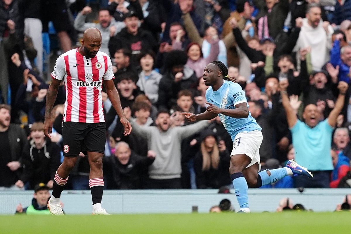 Manchester City winger Jérémy Doku celebrates with a pointed finger and a wide smile after scoring the opening goal in a 3-0 victory over Brentford on May 9, 2026. Beside him, a Brentford player in a red and white striped jersey, Igor Thiago, looks on as the Etihad Stadium crowd cheers in the background. Image used for Sportxparte news roundup.