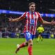 Atlético Madrid forward Julián Álvarez celebrates a goal on the pitch during a match. He wears the club's traditional red-and-white striped jersey with blue shorts emblazoned with the number 19. Image used for Sportxparte news.