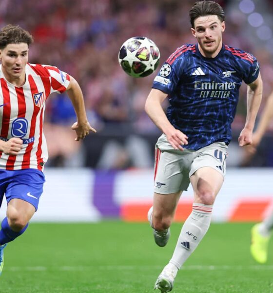 An action shot from a football match featuring Declan Rice of Arsenal and Julián Álvarez of Atlético Madrid competing for the ball. Rice, on the right, is wearing a dark blue and red Arsenal away kit, while Álvarez, on the left, is in Atlético’s traditional red-and-white striped home jersey. Image used for Sportxparte news Preview.