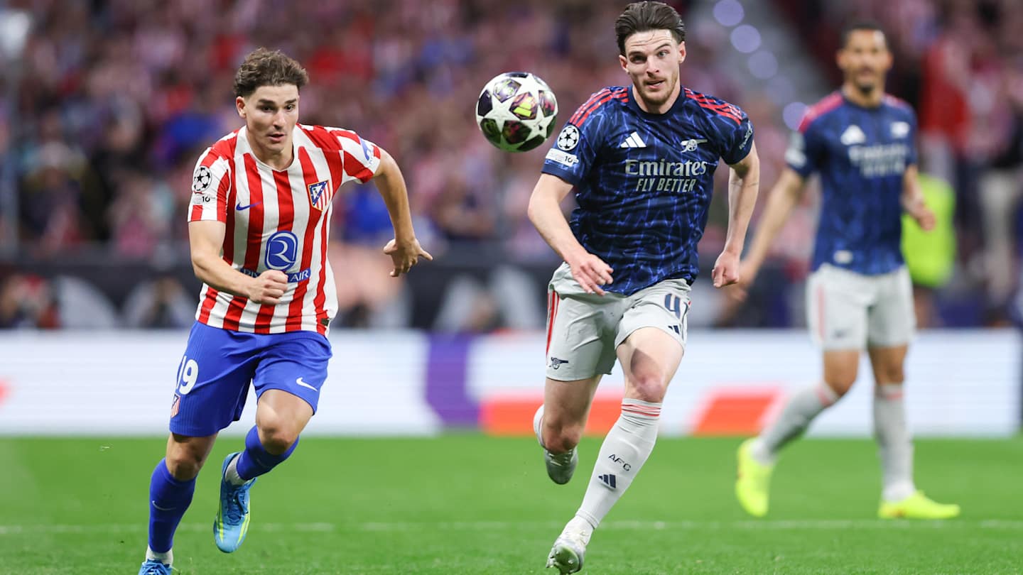 An action shot from a football match featuring Declan Rice of Arsenal and Julián Álvarez of Atlético Madrid competing for the ball. Rice, on the right, is wearing a dark blue and red Arsenal away kit, while Álvarez, on the left, is in Atlético’s traditional red-and-white striped home jersey. Image used for Sportxparte news Preview.