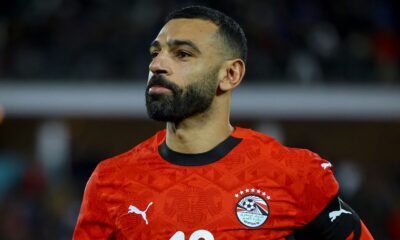 Mohamed Salah representing the Egyptian National Football Team. He is seen sporting a shorter hairstyle and trimmed beard while wearing the official Egyptian red Puma national jersey. Image used for Sportxparte news.