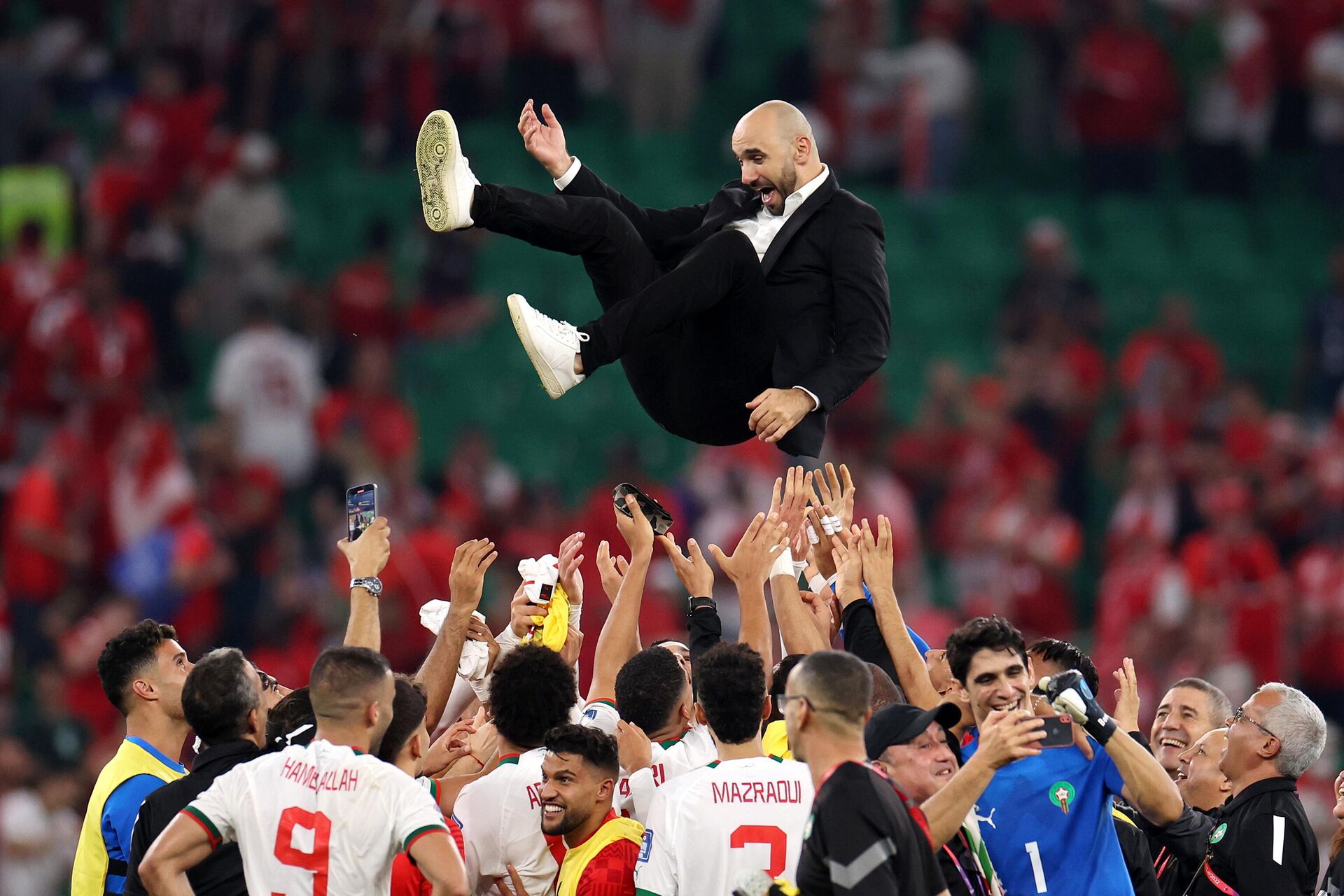 Moroccan national football team players enthusiastically throw their manager, Walid Regragui, into the air in celebration on the pitch. Image used for Sportxparte news.