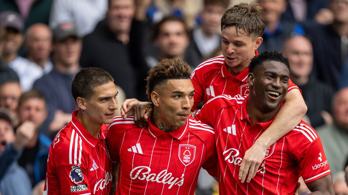 An image of four professional football players from Nottingham Forest celebrating a goal. They are wearing their red home kits with white pinstripes and "Bally's" sponsorship across the chest. From left to right, Nicolas Domínguez, Igor Jesus, James McAtee (background), and Taiwo Awoniyi are huddled together, smiling and embracing in a moment of triumph on the pitch, with a blurred crowd of fans in the background. Image used for Sportxparte news roundup.