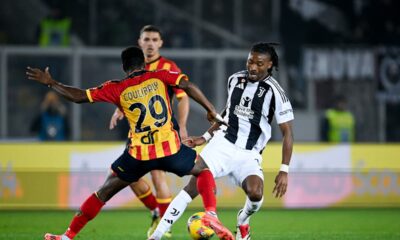 Serie A football match showing Khéphren Thuram of Juventus in a black-and-white striped jersey dribbling the ball. He is being closely defended from behind by Lameck Banda of US Lecce, who is wearing a yellow and red striped kit with the number 29. Image used for Sportxparte news.