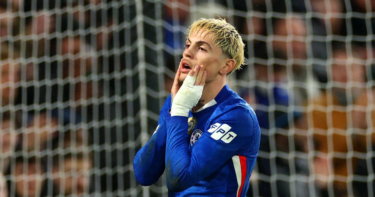 Alejandro Garnacho on the pitch, wearing a blue Chelsea FC jersey with a white sponsor logo on the sleeve. He has bleached blonde hair and a white supportive bandage wrapped tightly around his right hand, which he is pressing against his cheek with a stressed or contemplative facial expression. Image used for Sportxparte news.