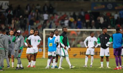 A group of players and staff from the Nigeria men's national football team, the Super Eagles, stand on a stadium pitch looking dejected or pensive. Image used for Sportxparte news.