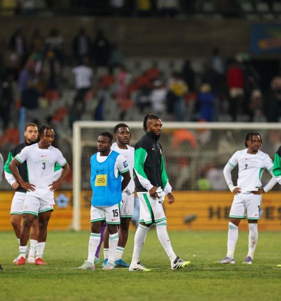 A group of players and staff from the Nigeria men's national football team, the Super Eagles, stand on a stadium pitch looking dejected or pensive. Image used for Sportxparte news.