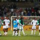 A group of players and staff from the Nigeria men's national football team, the Super Eagles, stand on a stadium pitch looking dejected or pensive. Image used for Sportxparte news.