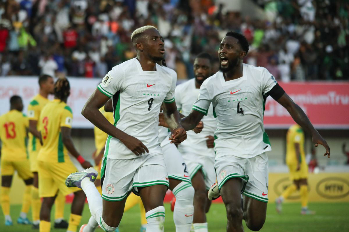 A close-up action shot of Victor Osimhen (number 9) and Wilfred Ndidi (number 4) celebrating a goal while wearing the white Nike Nigeria national football team kit during a match. Image used for Sportxparte news. 