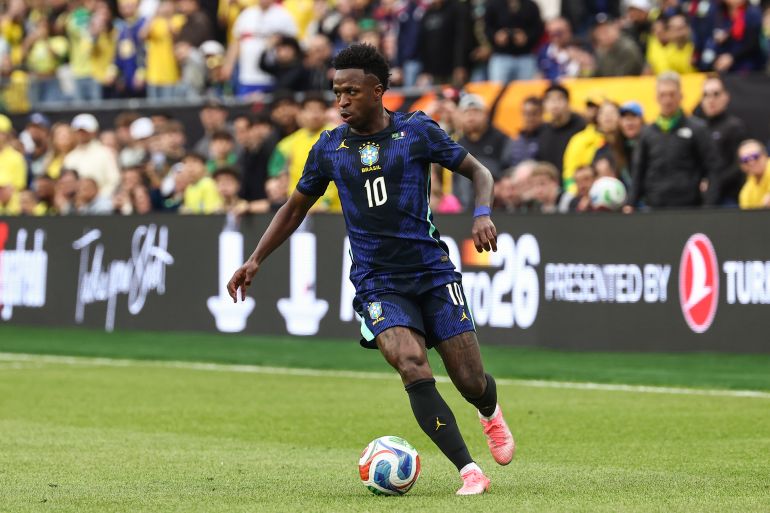 Vinícius Júnior is wearing the Jordan Brand Brazil away kit, a dark blue jersey featuring neon accents and the iconic Jumpman logo. Image used for Sportxparte news.