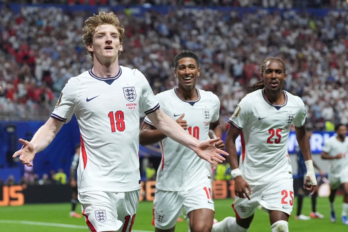 England national football players celebrate on the pitch during a stadium match. In the foreground, Anthony Gordon (#18) runs forward with a joyful expression and arms wide open. Behind him, Jude Bellingham (#10) smiles broadly. Image used for Sportxparte news.