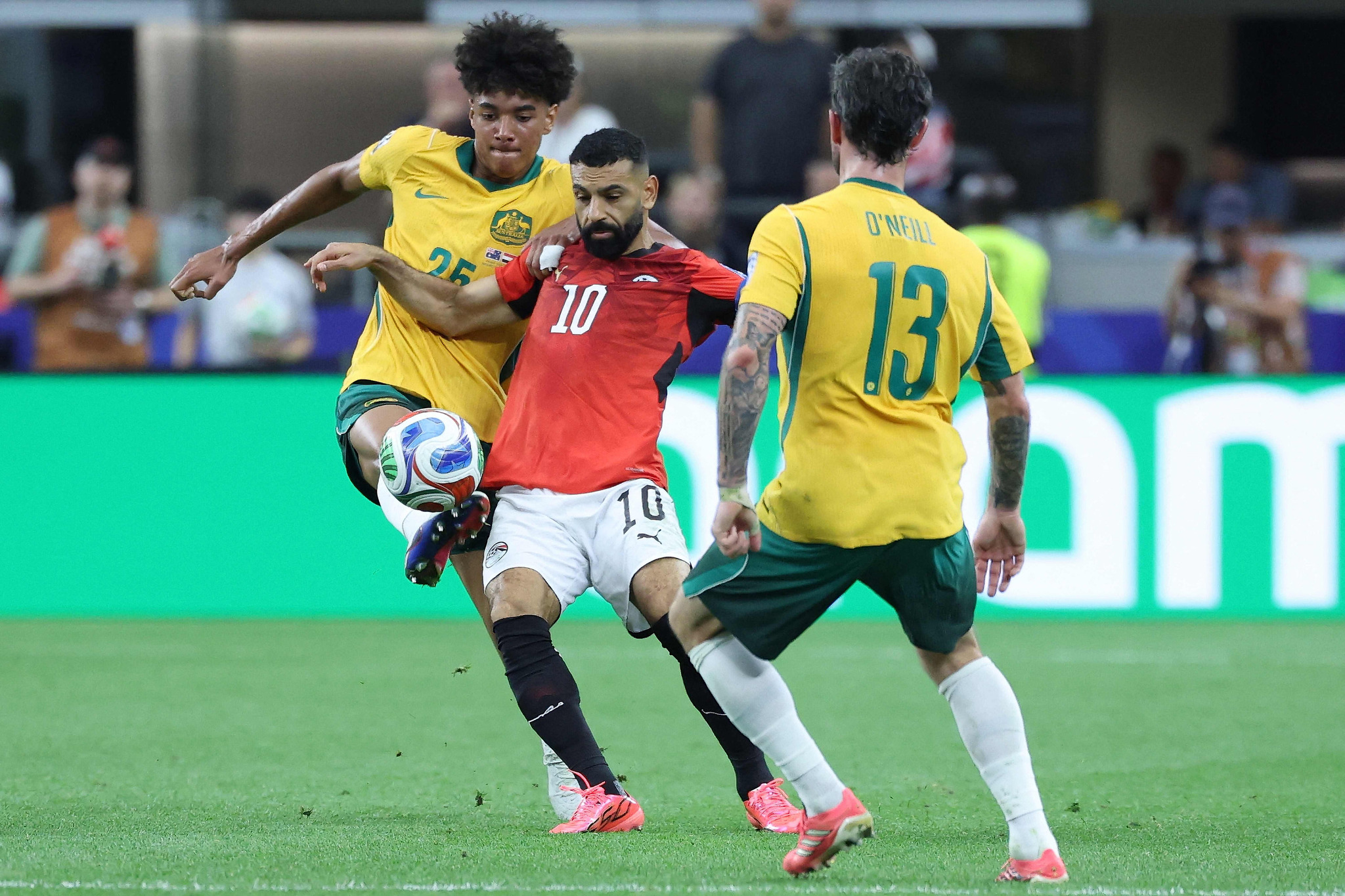 Mohamed Salah (wearing Egypt's number 10 jersey) is battling for possession against Australia's Lucas Herrington (number 25) and Aiden O'Neill (number 13). Image used for Sportxparte news.