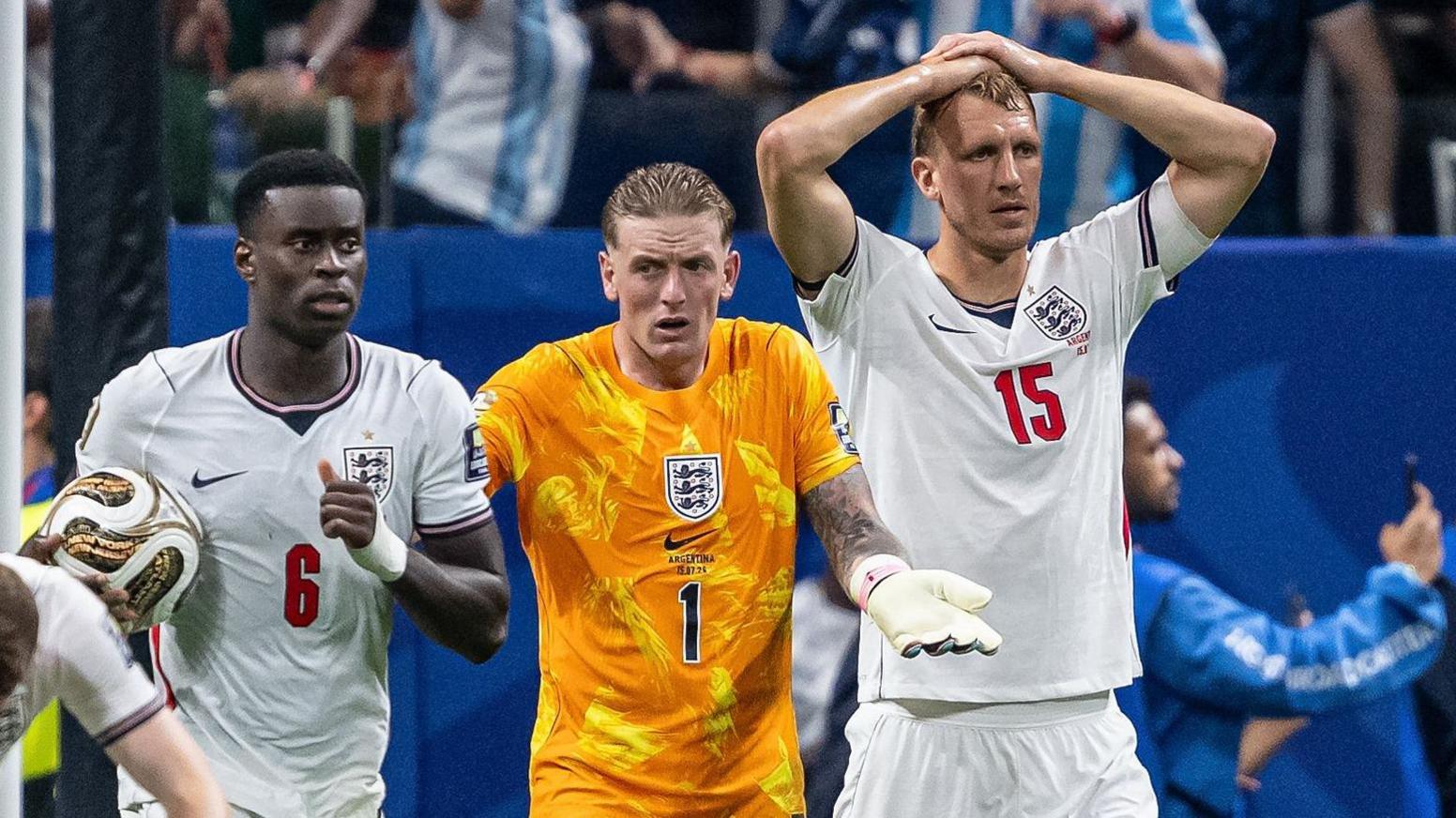 An England national football team player, Jordan Pickford, John Stones, and Marc Guéhi react with heartbreak and dejection on the pitch following their 2-1 defeat to Argentina in the 2026 FIFA World Cup semi-finals. Image used for Sportxparte news.