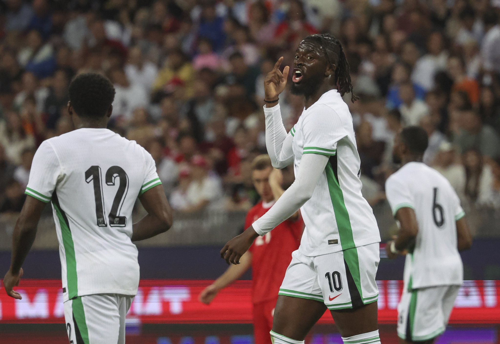 Tolu Arokodare is pictured in the center wearing jersey number 10 for the Nigeria national football team, celebrating his decisive goal in a 1-0 victory over Rwanda. The match took place on September 6, 2025, at the Godswill Akpabio International Stadium in Uyo during the 2026 FIFA World Cup qualifiers. Image used for Sportxparte news.