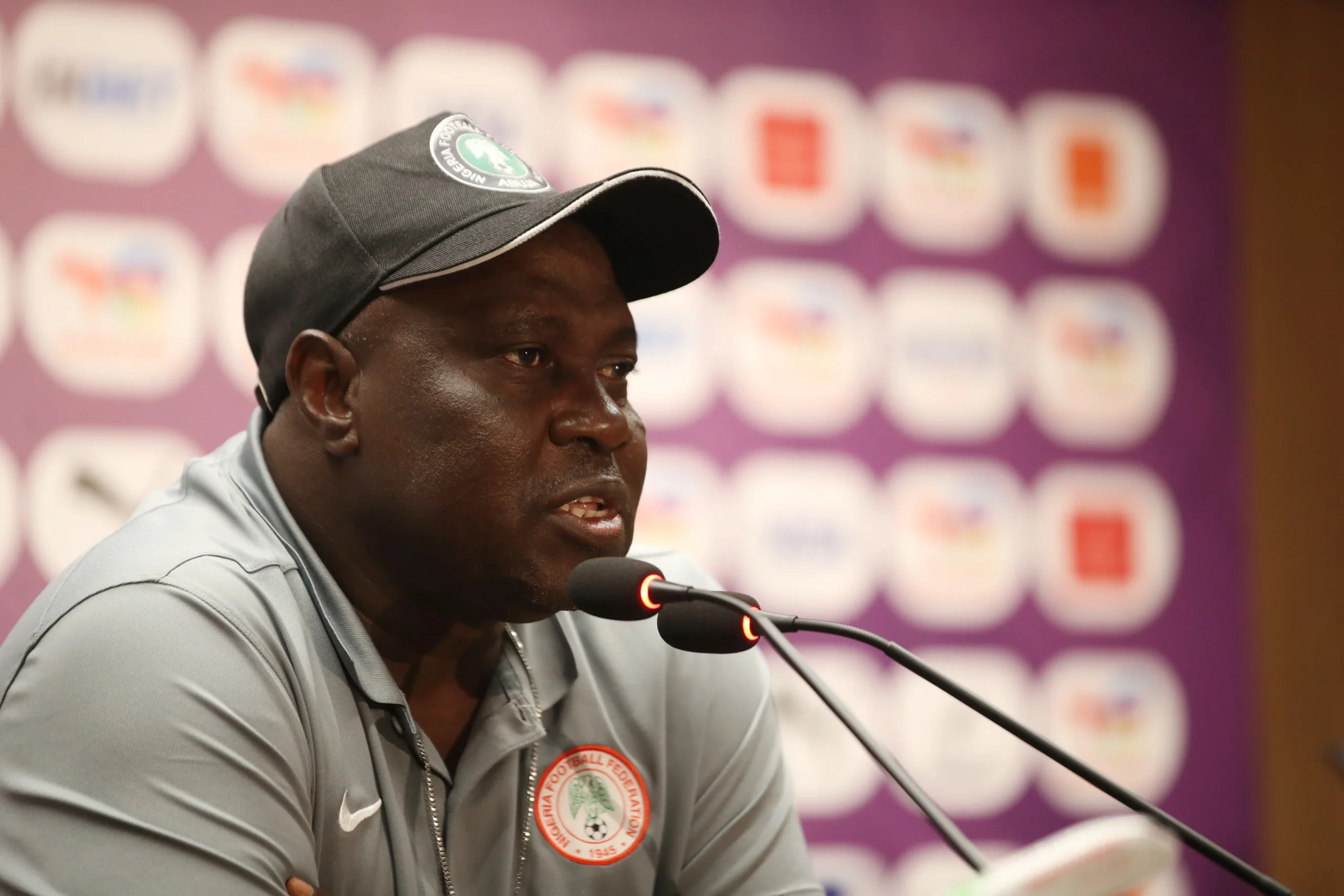 Justin Madugu, the head coach of Nigeria's women's national football team (the Super Falcons), speaking into a microphone during a press conference. Image used for Sportxparte news.