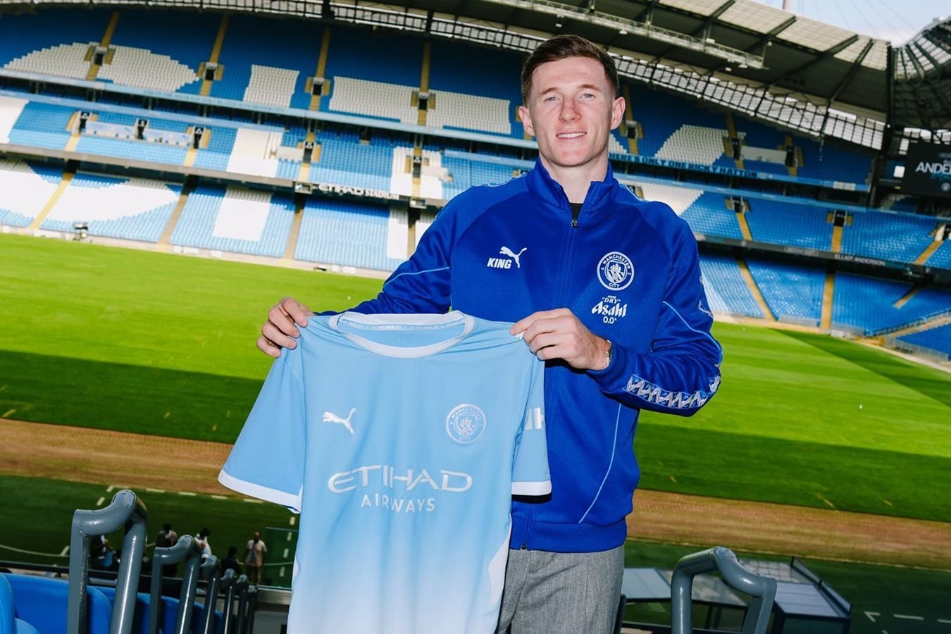 Elliot Anderson holding up a Manchester City home shirt during his official transfer unveiling at the Etihad Stadium. Image used for Sportxparte news.